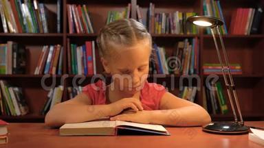 一个六岁的女孩坐在桌旁的台灯旁看书